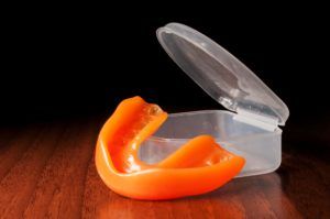 Orange sports mouth guard next to a protective case on a wood floor and a black background