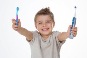 boy holding a manual toothbrush in his right hand and an electric toothbrush in his left hand